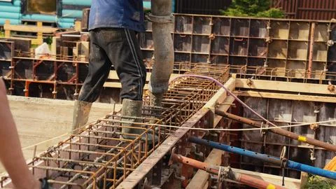 Construction worker pouring concrete into building foundation rebar frame Stock Photos