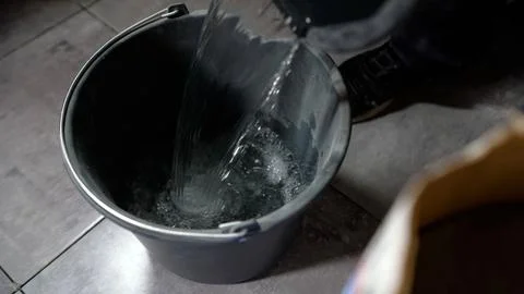Construction worker pouring fresh water from container into black bucket fo.. Stock Photos