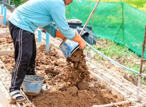 A construction worker pours sand or soil into a foundation trench using a b.. Stock Photos