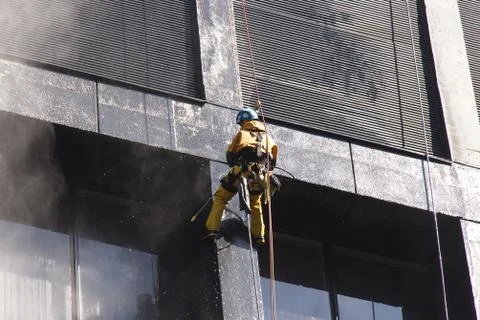 Construction worker power washes windows one of the office buildings Stock Photos