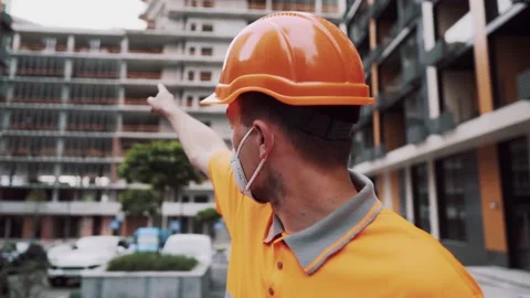 Construction worker in protective helmet, mask and orange uniform is discussing Stock Footage 155077352