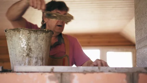 A construction worker is putting a layer of cement on the brick wall, smiling Stock Footage 90097371