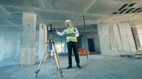 Construction worker is regulating land surveying equipment at a construction Video stock 95680085