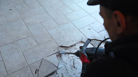 Construction worker removes cracked ceramic floor tiles using a power tool Stock Footage 322541692