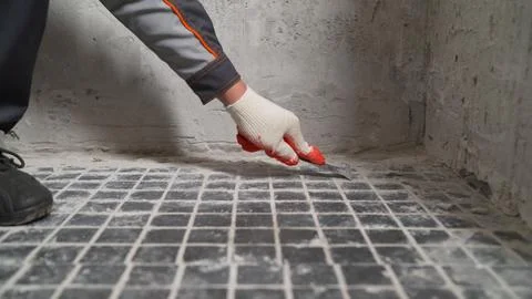 Construction worker removing grout from tiles with a scraper Stock Photos