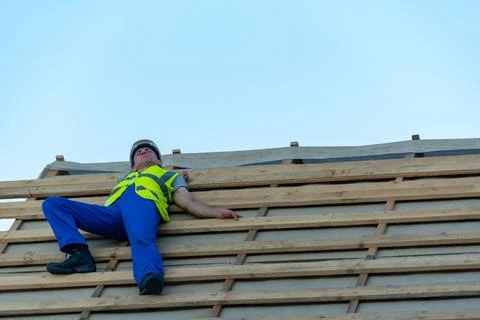 Construction worker in safety gear collapsed on a roof under construction, .. Stock Photos