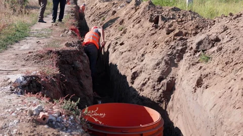 Construction worker in safety gear is digging a trench for water system Stock Footage 318714761