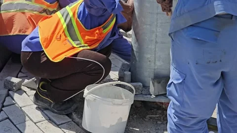 Construction worker in safety vest and gloves crouches, pouring material into a Stock Footage 311764739
