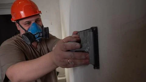 Construction worker sanding a plastered wall surface with a sanding block and Stock Photos
