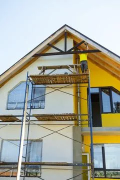Construction worker on scaffold uses hammer installing decorative timber on.. Stock Photos
