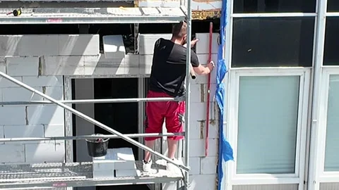 Construction worker on scaffolding installing window frame on building exterior. Stock Footage 337985517