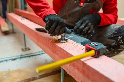 Construction worker screws bolts up tight on the stud on the wooden block in Stock Photos