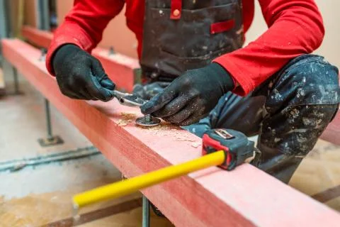 Construction worker screws bolts up tight on the stud on the wooden block in Stock Photos