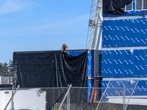 Construction worker securing black tarp over blue insulation on rising Фото