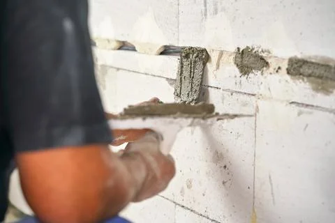 Construction worker securing electric sockets groove installed on bare wall.. Stock Photos