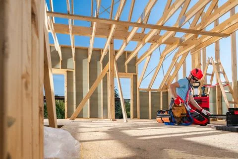 Construction Worker Securing Wooden Beams Inside a New Home Under Bright Bl.. 写真素材