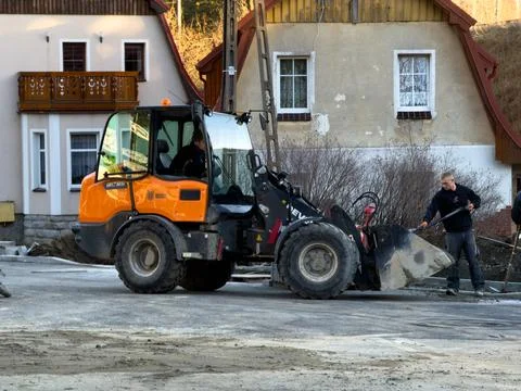 A construction worker with a shovel operates a wheel loader on a residential Stock Photos