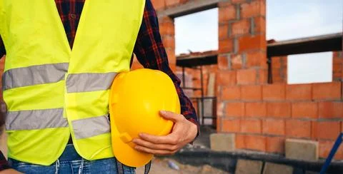 Construction worker on site zone. Worker in yellow vest holding hard hat. Stock Photos