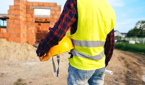 Construction worker on site zone. Worker in yellow vest holding hard hat. Stock Photos