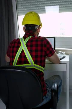 Construction Worker is sitting at his desk at the computer Stock Photos