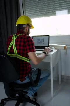 Construction Worker is sitting at his desk at the computer Stock Photos