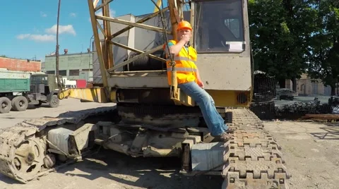 Construction worker sitting on large crawler cranes and eating an apple. Video stock 52251162