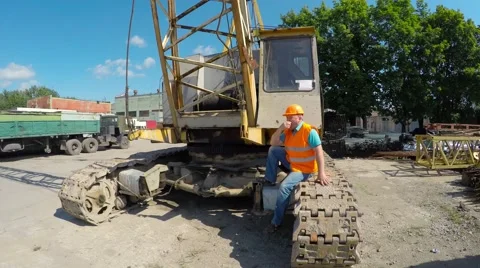 Construction worker sitting on large crawler cranes and eating an apple. Video stock 52251250