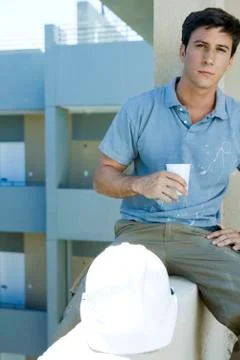 Construction worker sitting on ledge holding drink taking break Stock Photos