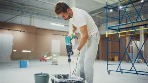 A construction worker skillfully mixes paint with a power drill, preparing for a Видео 316050705