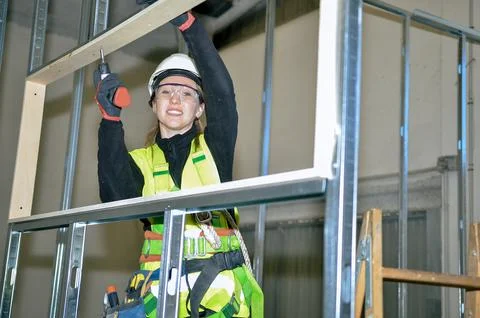 Construction worker smiling and mounting plasterboard on metal frame Stock Photos