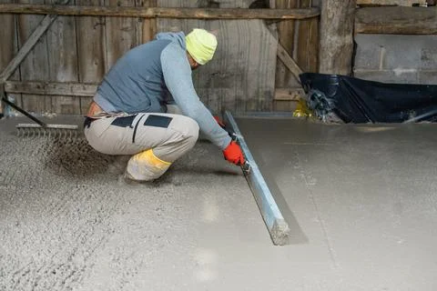 Construction Worker Smoothing Concrete Surface with Leveler in Barn, Perfect for Stock Photos