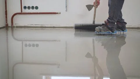 Construction worker in spiked shoes leveling wet self-leveling screed on a .. Stock Photos