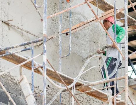 Construction worker spraying cement plaster on an exterior wall while stand.. Stock Photos