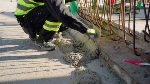 Construction worker spreading concrete across metal frame, wearing protective Stock Footage 306393681