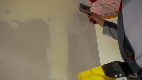 Construction worker spreading joint compound on drywall near electrical outlet Stock Footage 320142732