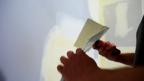 Construction worker spreading joint compound on the drywall wall using a metal Stock Footage 320143546