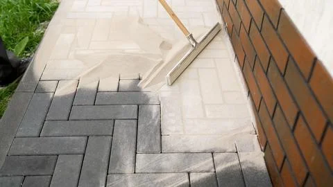 Construction worker spreading sand on paving stones with brick wall Stock Photos