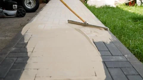 Construction worker spreading sand on paving stones Foto stock