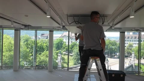 Construction worker standing on ladder installs ceiling element inside modern Stock Footage 331304649