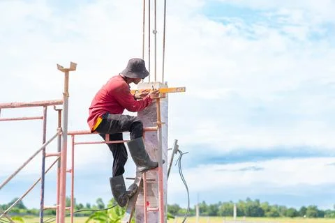 A construction worker is standing on scaffolding, using a spirit level to m.. Stock Photos