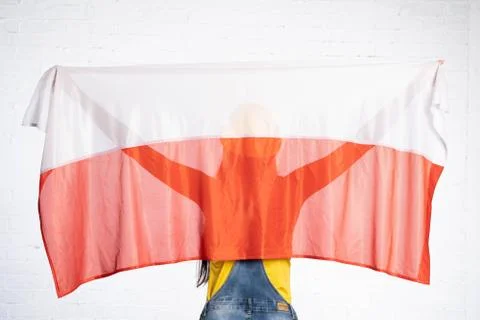 A construction worker stands back to the lens and holds the Polish national flag 写真素材