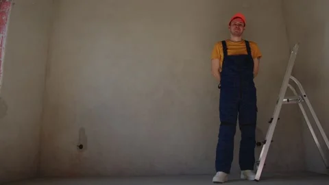 A construction worker stands with a ladder in an empty room ready for drywall Stock Footage 306181450