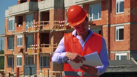 Construction worker studies some documents in front of building site Stock Footage 79050642