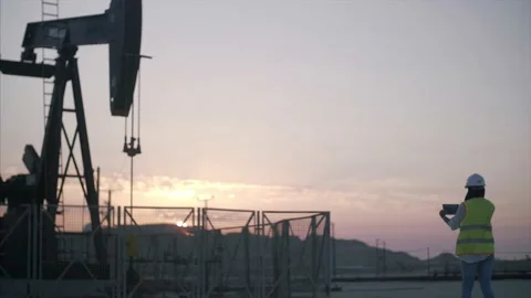 Construction worker surveys oil rig with device at sunrise. Stock Footage 157398651
