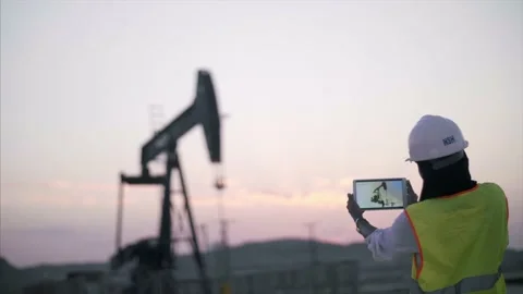 Construction worker surveys oil rig with device at sunrise. Stock Footage 157398681