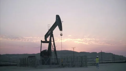 Construction worker surveys oil rig with device at sunrise. Stock Footage 157398973