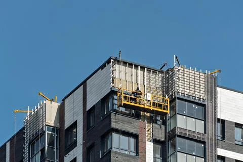 Construction worker on suspended platform repairs high-rise building facade Stock Photos