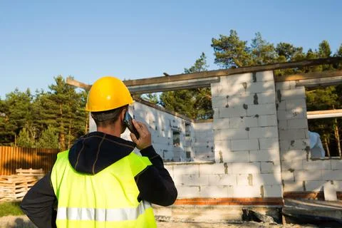 Construction worker talks on a smartphone in a yellow hardhat and reflective  Stock-Fotos