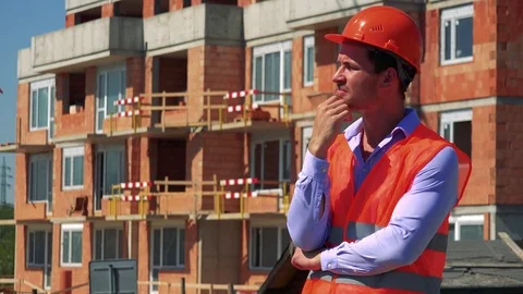 Construction worker thinks about something in front of building site 스톡 동영상 79050544