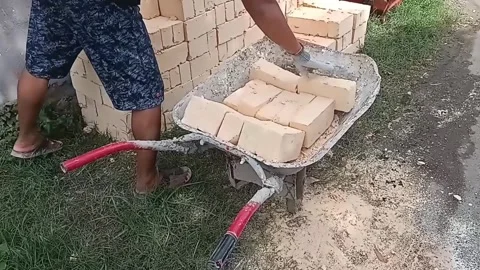 A construction worker is transporting or placing bricks into a wheelbarrow Stock Footage 298160263